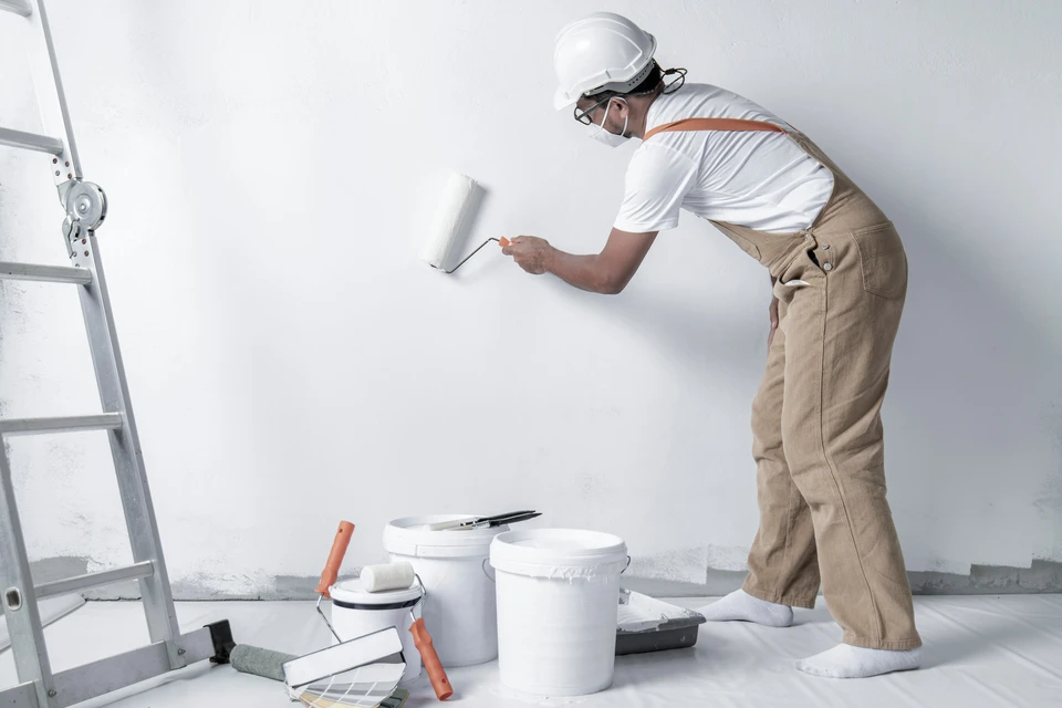 Peintre professionnel appliquant de la peinture murale blanche avec un rouleau dans un espace intérieur