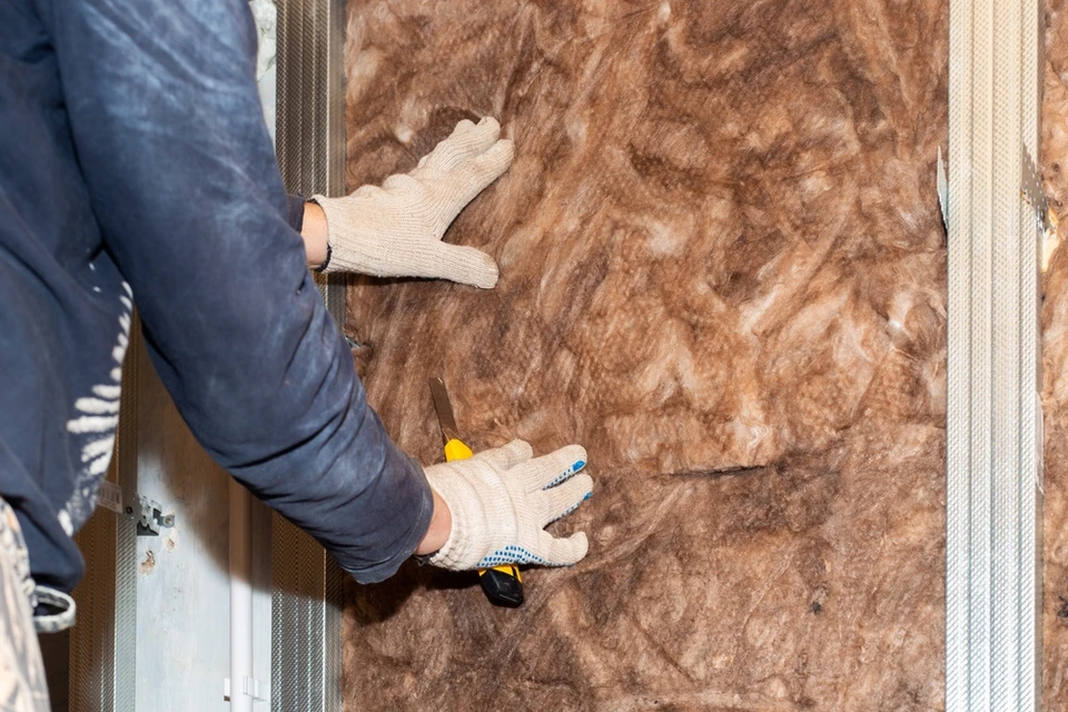 Ouvrier en vêtements de travail bleus et gants de protection blancs installant un panneau d'isolation thermique de couleur brun-orangé sur une façade extérieure