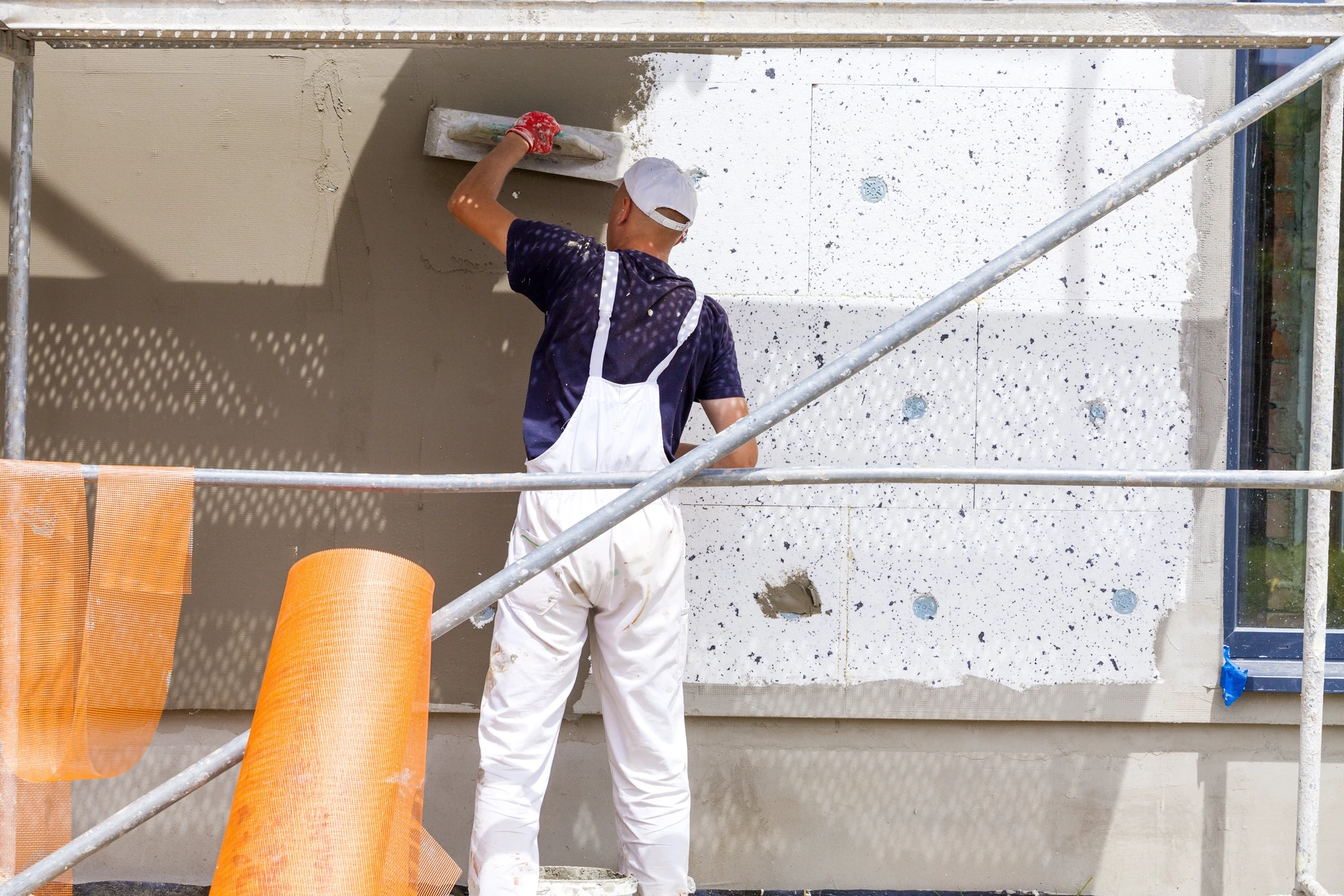 Ouvrier en bâtiment appliquant un enduit de façade sur mur extérieur depuis échafaudage