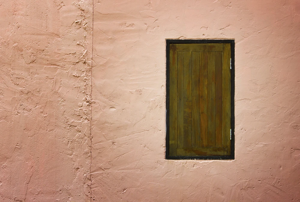 Façade extérieure d'un bâtiment avec mur en crépi rose saumon présentant des fissures et imperfections