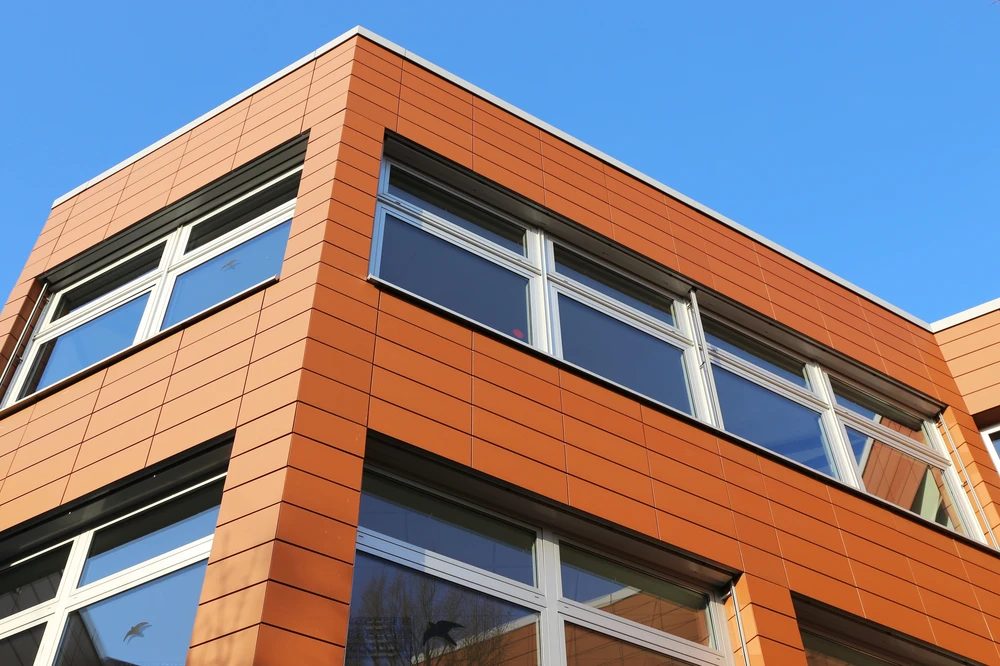 Façade extérieure d'un bâtiment moderne à deux étages avec bardage en panneaux de terre cuite orange disposés en quinconce