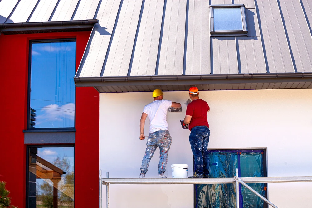 Deux ouvriers en bâtiment travaillent sur échafaudage, appliquant un enduit mural extérieur à la main