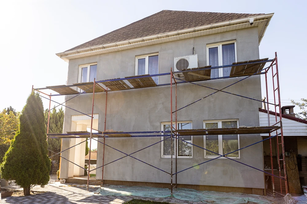 Chantier de rénovation extérieure d'une maison individuelle à deux étages avec échafaudage métallique rouge installé sur la façade