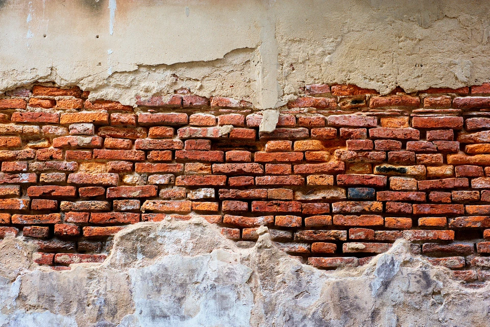 Mur extérieur ancien en détérioration montrant une maçonnerie de briques rouges apparentes sous un enduit de façade écaillé et fissuré