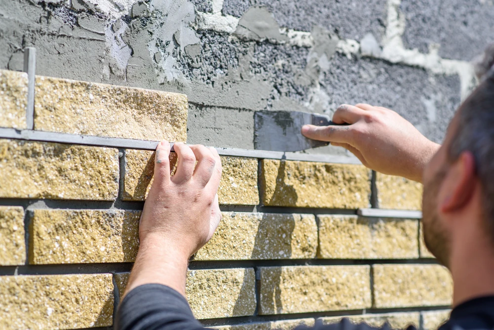 Ouvrier en construction appliquant du mortier sur un mur en briques jaunes à l'aide d'une truelle