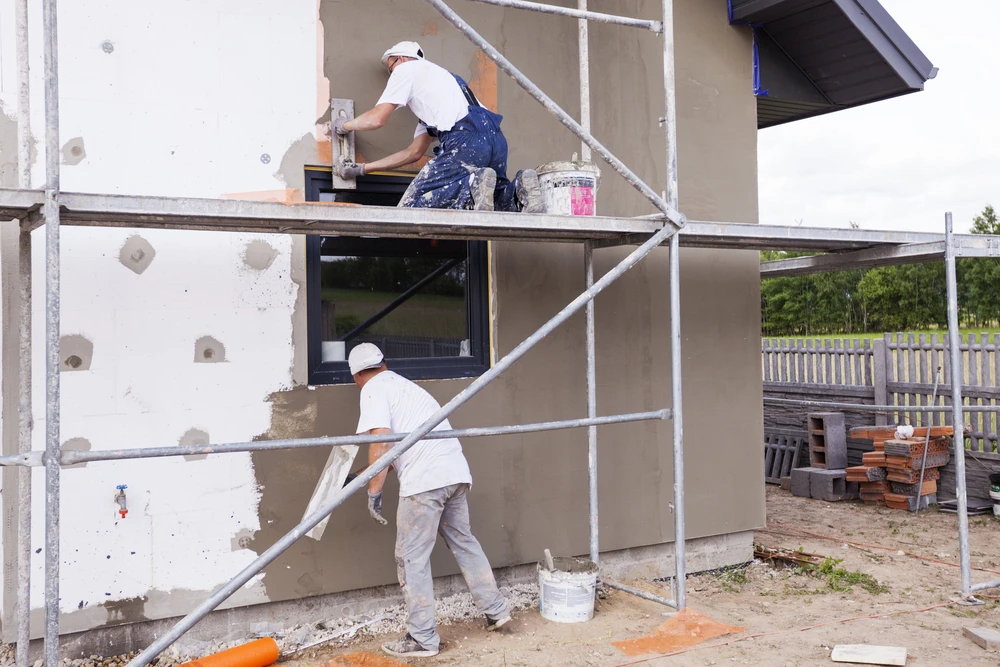 Chantier de construction résidentielle en extérieur avec deux ouvriers appliquant un enduit de façade