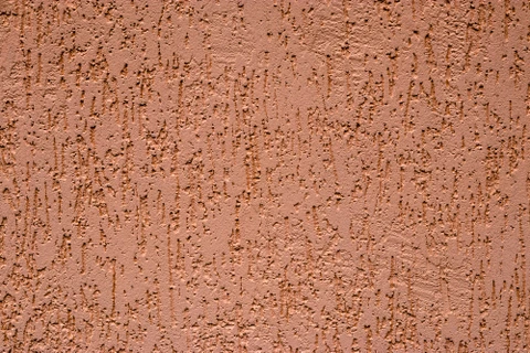 Mur extérieur en crépi taloché de couleur terre cuite, présentant une finition rustique avec relief granuleux